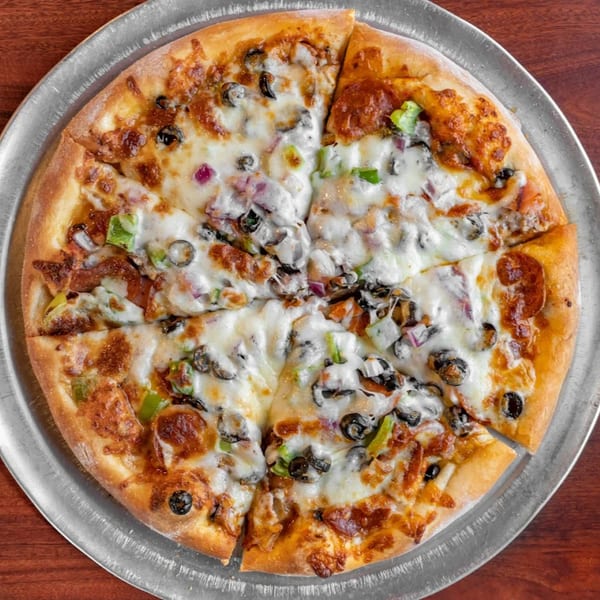 A whole Pizza Bella pizza with pepperoni, olives, green peppers, and onions on a metal tray.