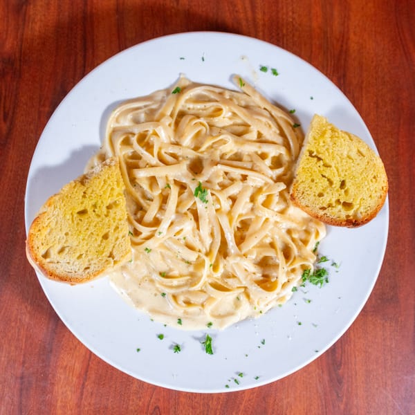 Creamy fettuccine alfredo pasta with parsley and two slices of garlic bread on a white plate.