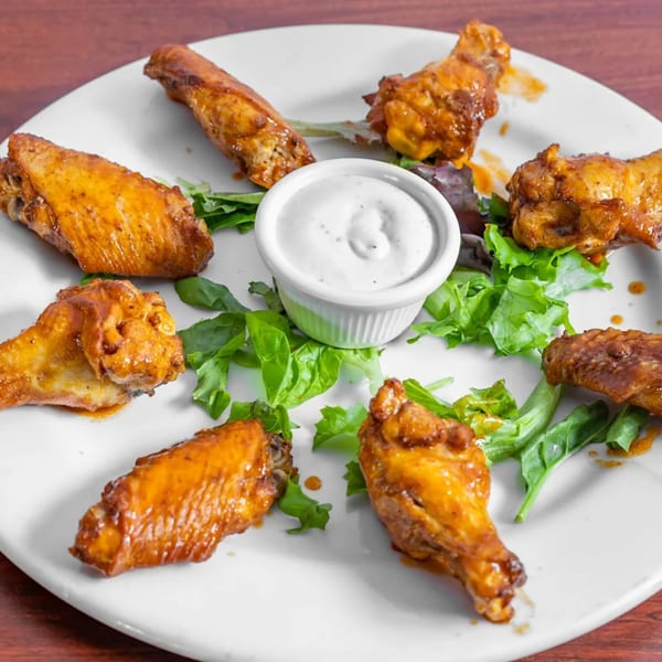 A plate of eight golden-brown chicken wings with a side of ranch dressing and green lettuce.