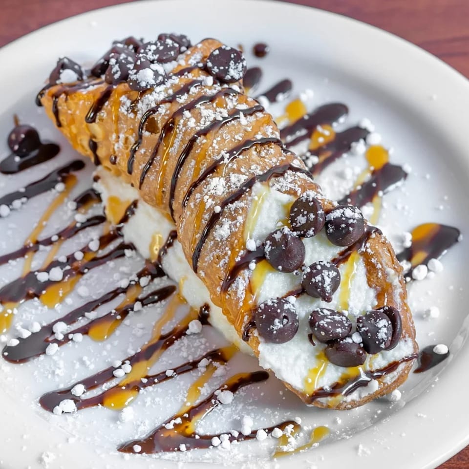 A cannoli from Pizza Bella Italian Bistro, drizzled with chocolate and caramel, topped with chocolate chips and powdered sugar.